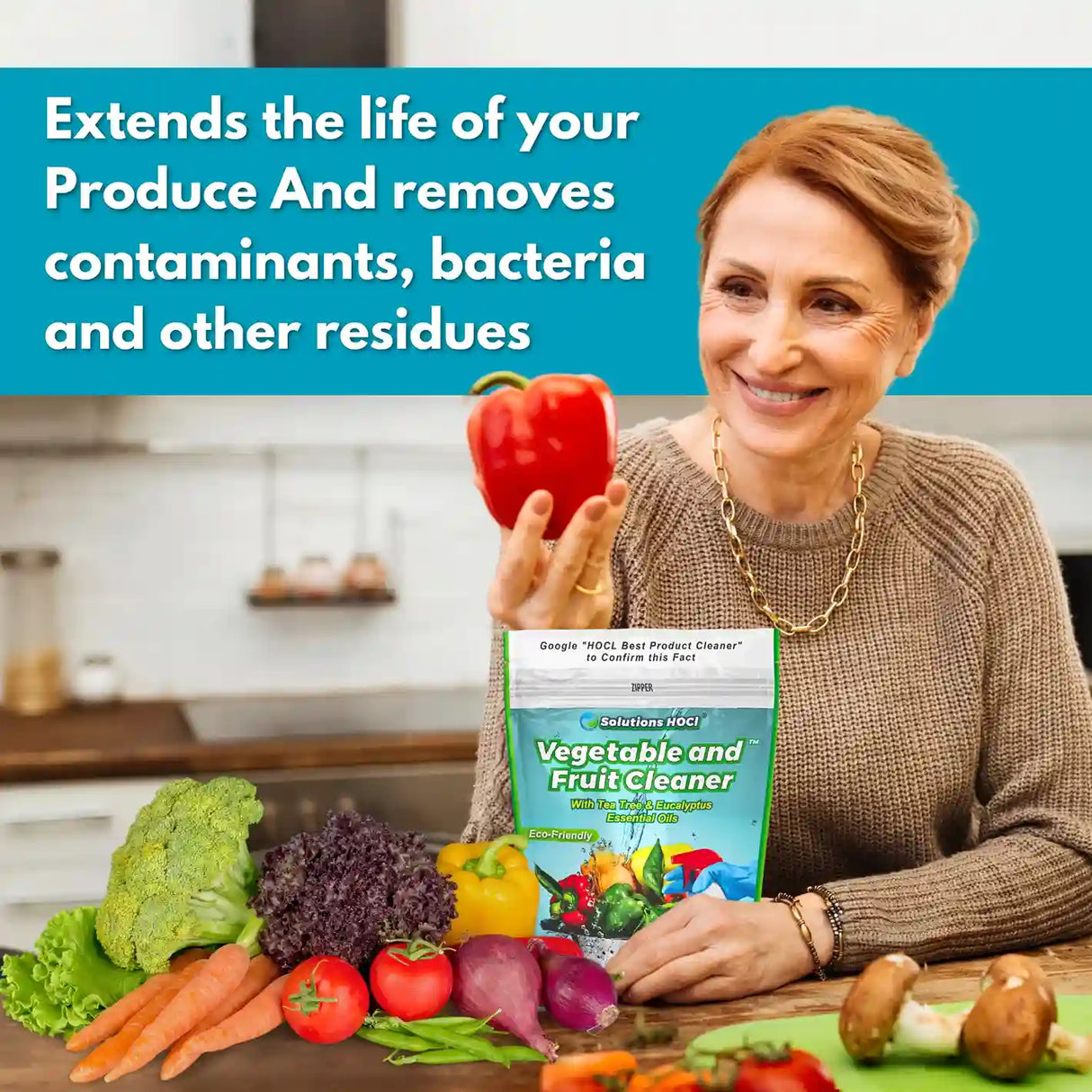Woman holding a red pepper with a vegetable and fruit cleaner box, surrounded by fresh produce in a kitchen.