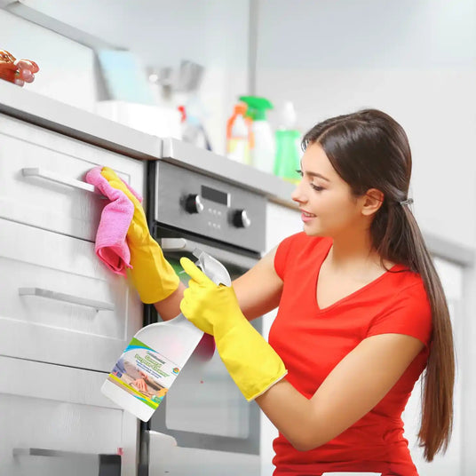 Woman cleaning a kitchen cabinet with gloves on, holding a cleaning product.