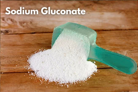 White powder in a green scoop on a wooden surface with 'Sodium Gluconate' text.